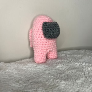 May include: Pink crocheted plush toy shaped like the character from the video game Among Us. The toy has a gray visor.