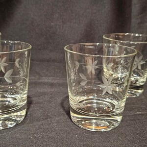 May include: Four clear glass tumblers with an etched floral design. The glasses are on a dark surface.