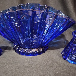 May include: A set of three cobalt blue glass pieces, including a fan-shaped bowl and two candle holders. The pieces are all decorated with a geometric pattern.