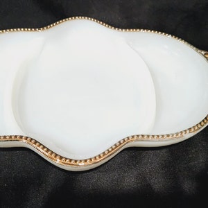 May include: A white, three-section serving dish with a gold beaded trim. The dish has a unique, wavy shape and is ideal for serving appetizers or snacks. The gold trim adds a touch of elegance to the serving piece.