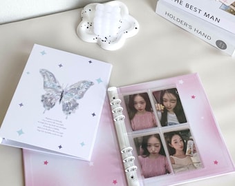 May include: A white photo album with a butterfly design and a quote about happiness. The album has a ring binder and is open to reveal clear plastic photo sleeves with pictures of women.