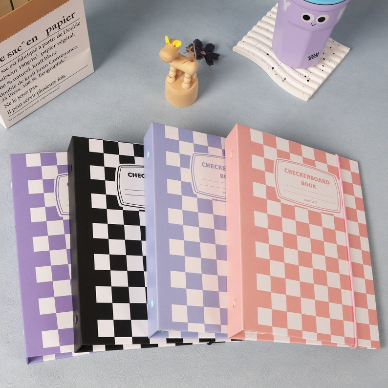 May include: Four checkerboard patterned binders in different colors: purple, black, light purple, and pink. The binders have a label that says "Checkerboard Book".