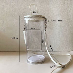 May include: Clear cylindrical handbag with white accents. Features a white handle, a zipper closure, and a detachable white shoulder strap. The bag is 15.5 inches tall, 8.6 inches wide, and the strap is adjustable from 37.40 to 42.12 inches.