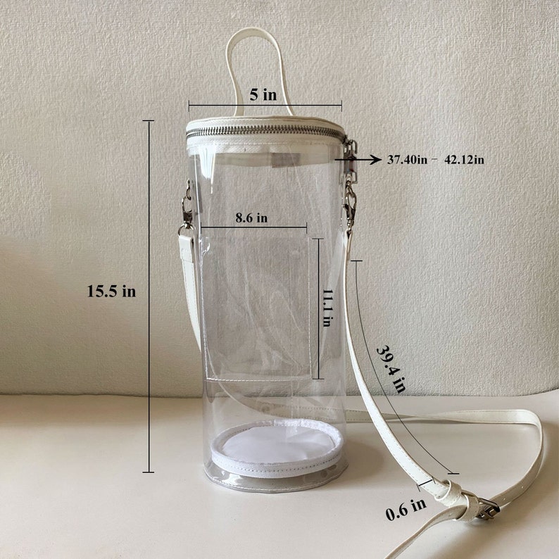 May include: Clear cylindrical handbag with white accents. Features a white handle, a zipper closure, and a detachable white shoulder strap. The bag is 15.5 inches tall, 8.6 inches wide, and the strap is adjustable from 37.40 to 42.12 inches.
