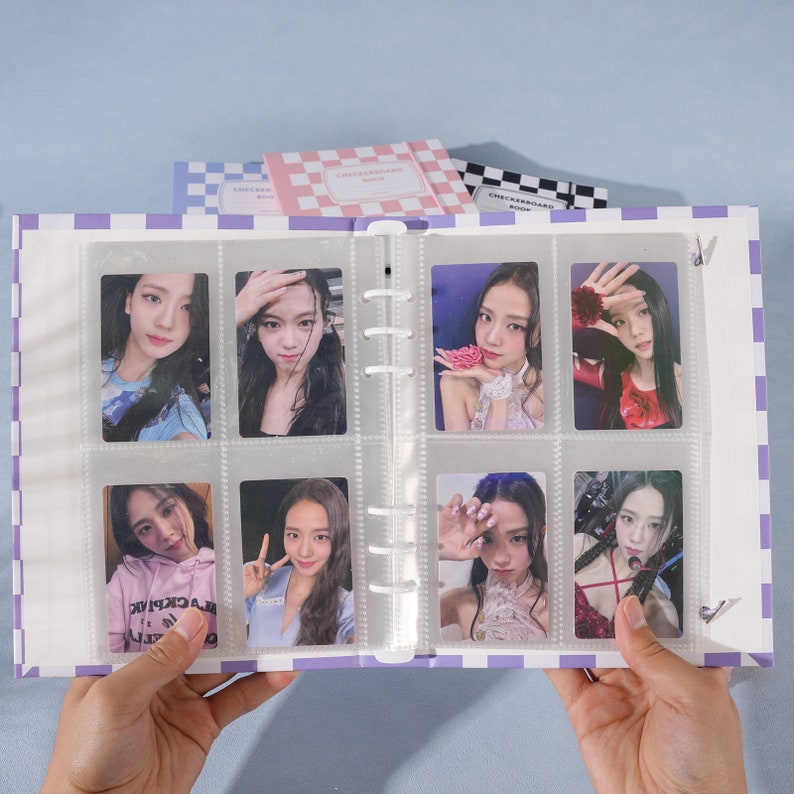 May include: A purple and white checkered binder with clear plastic sleeves holding photo cards of a K-pop group. The binder has a metal ring binding system.