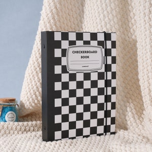 May include: Black and white checkered notebook with a black spine and a black elastic band closure. The cover has the text "Checkerboard Book" in white lettering.