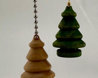 May include: Two Christmas tree-shaped light pull chains. One is natural wood-toned, the other is green. Both are suspended by a metal ball chain. The tree shapes have a tiered design, and are likely made of wood.