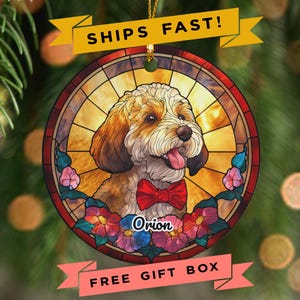 May include: Round dog ornament with a stained-glass design. The ornament features a portrait of a dog wearing a red bow tie, surrounded by flowers. The name "Orion" is written on the ornament. The ornament has a gold string for hanging.