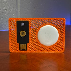 May include: An orange plastic card with a black USB drive and a white round button. The card has a grid pattern.