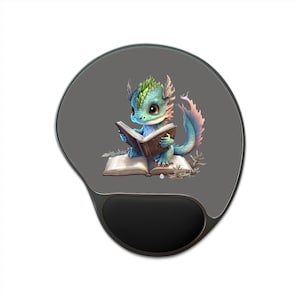 May include: A dark gray ergonomic mouse pad with a black wrist rest, featuring a central illustration of a small, teal-colored dragon with green scales and a pink-tipped tail, sitting and reading an open brown book on top of another open book.