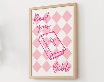Può includere: Una stampa incorniciata con uno sfondo a motivo a rombi rosa e bianchi. La stampa presenta un'illustrazione in rosa di una Bibbia con una croce e le parole "Read your Bible" in corsivo rosa. La cornice è di colore legno chiaro.
