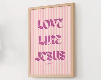Può includere: Stampa artistica incorniciata con la scritta "LOVE LIKE JESUS" in corsivo viola su sfondo a righe rosa e bianche. Il versetto biblico Giovanni 13:34 è stampato sotto. La cornice è di colore legno chiaro.