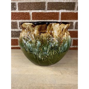 May include: A ceramic planter with a textured, leaf-like design. The planter features a dark brown rim, transitioning to tan and green hues. The base is a deep green, creating a layered, earthy aesthetic. Ideal for indoor or outdoor use.