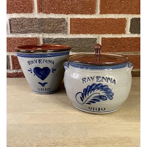 Puede incluir: Dos piezas de cerámica de gres. Un cuenco pequeño con un diseño de corazón azul y las palabras "Ravenna" y "Ohio". Un tarro redondo con tapa, un diseño de hoja azul y las palabras "Ravenna" y "Ohio".