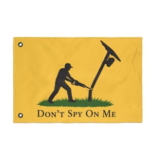 May include: A rectangular yellow flag with two metal grommets on the left side. The center features a black silhouette of a person cutting down a utility pole with a saw, standing on green grass. The text DON'T SPY ON ME is printed in black.