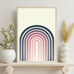 Op de afbeelding: Een ingelijste kunstdruk met een gestileerde regenboog in marine-, paarse en roze tinten tegen een crèmekleurige achtergrond. Het kunstwerk wordt getoond op een licht houten plank, met witte vazen met decoratieve planten.