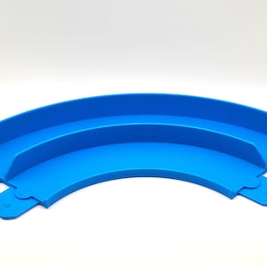 May include: A blue plastic track piece for a toy train set. The piece is curved and has two levels.