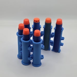 May include: A set of blue plastic modular holders for foam darts, each featuring a cylindrical design with side connectors. The holders contain dark blue foam darts with bright orange tips, including one dart with a perforated orange tip.
