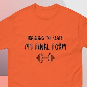May include: Orange t-shirt with the text "TRAINING TO REACH MY FINAL FORM" in black, along with a dumbbell graphic. The shirt is a solid orange color and has a crew neck.