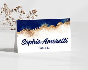 May include: A folded place card with a navy blue and gold watercolor design. The card features the name "Sophia Ameretti" in a cursive font, with "Table 13" below. The background has a white base.