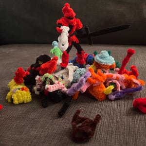 May include: A collection of colorful pipe cleaner figures, including a red knight with a sword, a blue hat, and a variety of other shapes and colors.