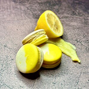May include: Four yellow and white macarons with a lemon wedge on a gray textured surface.