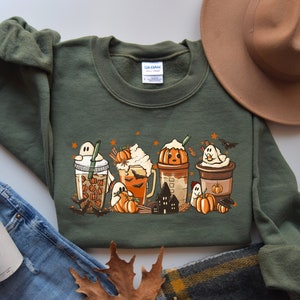 Op de afbeelding: Groen sweatshirt met een afbeelding van vijf Halloween-thema koffie drankjes met geesten, vleermuizen, pompoenen en sterren.