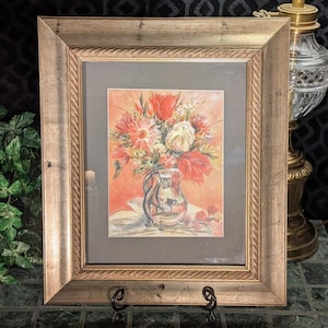 Può includere: Dipinto floreale ad acquerello incorniciato. L'opera presenta un bouquet di fiori rossi, bianchi e rosa in una brocca d'argento. Il dipinto è ambientato su uno sfondo color pesca e incorniciato in una cornice di legno dorato.