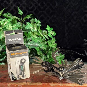 May include: A Topeak McGuyver 33 function folding tool with a black and silver finish. The tool is displayed next to its original box, which features the Topeak logo and the words "McGuyver 33 Function Folding Tool".