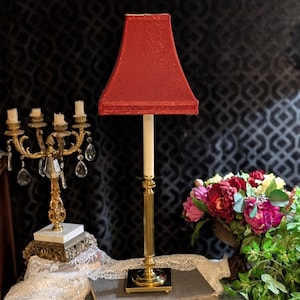 Könnte beinhalten: Eine hohe Tischlampe mit einem schlanken, kannelierten Messingfuß, einem quadratischen schwarzen Sockel und einem roten Stofflampenschirm. Der Schirm weist ein dezentes, geprägtes Blumenmuster auf. Die Lampe steht aufrecht mit einer geraden Säule.