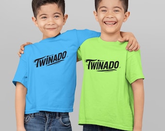 May include: Two young boys wearing matching t-shirts with the word "Twinado" in black. One shirt is light blue, the other is lime green. Both boys are wearing blue jeans and smiling.