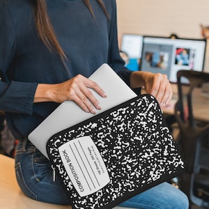 Puede incluir: Una funda para portátil negra y blanca con forma de cuaderno de composición con cremallera. La funda tiene el texto "COMPOSITION BOOK", "100 Sheets 200 Pages" y "9 x 7 1/4 in (24.7 cm x 18 cm)".