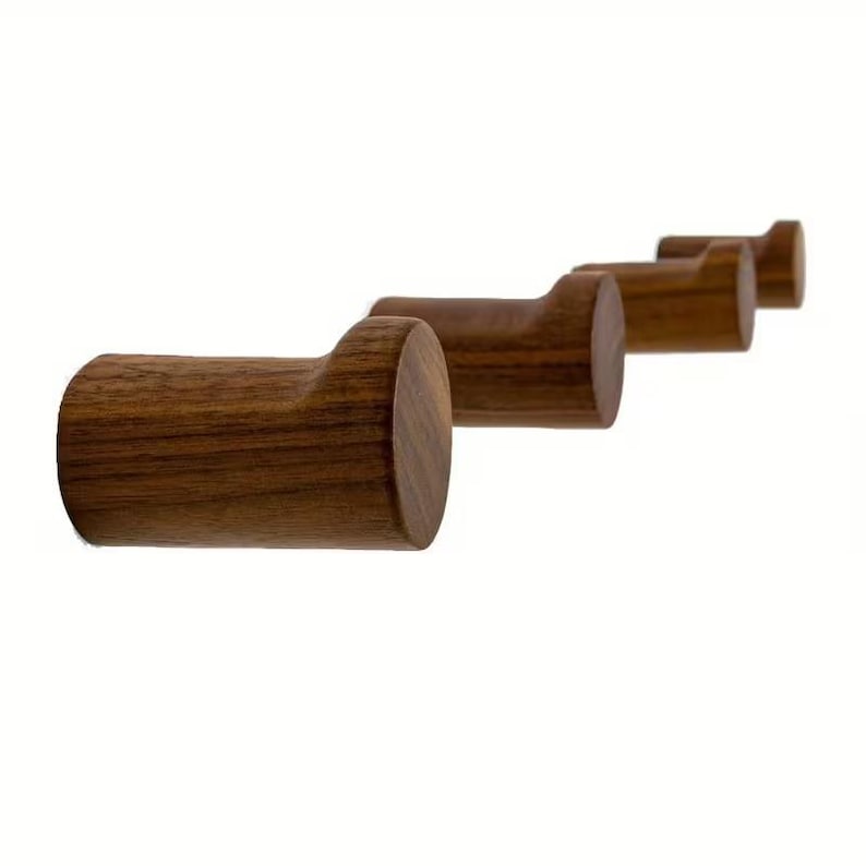 May include: A row of four wooden wall hooks. Each hook is cylindrical with a curved top, and they are arranged in a diagonal line. The hooks are made of a warm brown wood and are set against a white background.