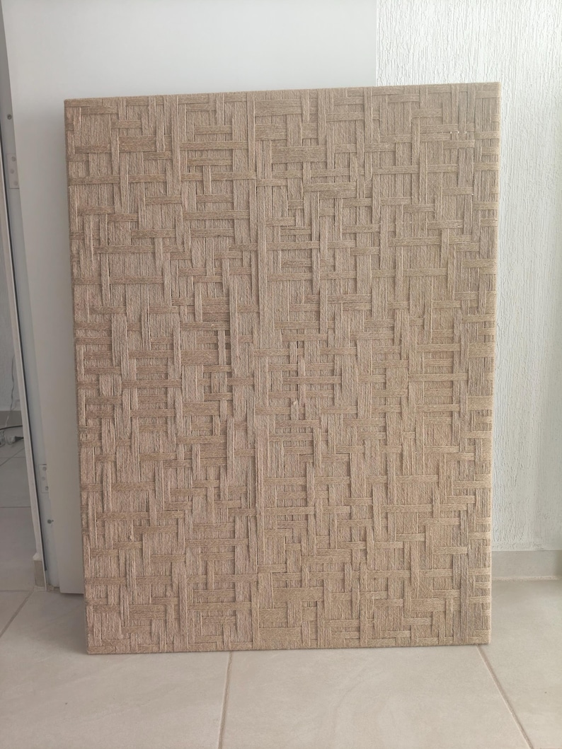 May include: A rectangular panel with a woven texture in shades of beige and tan. The pattern is a tight weave, creating a grid-like design. The panel is standing upright against a white wall.