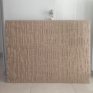 May include: A rectangular woven wall panel with a repeating pattern of interwoven beige fibers. The panel is mounted on a wall, and the texture is visible. The panel is a neutral color and could be used as a decorative element.