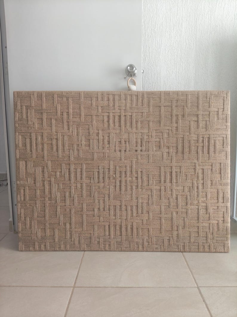 May include: A rectangular woven wall panel with a repeating pattern of interwoven beige fibers. The panel is mounted on a wall, and the texture is visible. The panel is a neutral color and could be used as a decorative element.