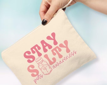 Pode incluir: Uma bolsa de lona bege com um gráfico rosa e branco que diz "Stay Salty" com uma ilustração de um saleiro e as palavras "pots awareness".