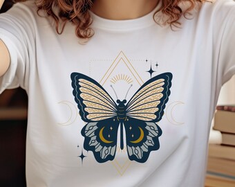 以下が含まれることがあります： 金色と青色の蝶のグラフィックが描かれた白いTシャツ。蝶は三日月と星に囲まれています。