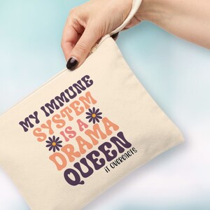 May include: A beige canvas zippered pouch with a pink and orange graphic that says "My Immune System is a Drama Queen It Overreacts".