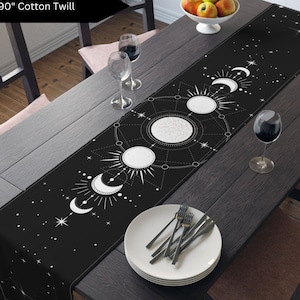 May include: A black table runner with a white moon and star design. The runner is 16 inches by 90 inches and is made of cotton twill.