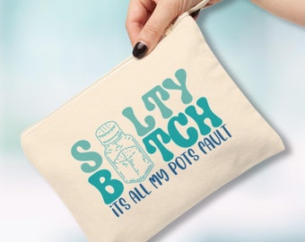 Pode incluir: Uma bolsa de lona bege com um design azul e verde que diz "Salty Bitch It's All My Pots Fault". A bolsa tem um fecho de correr e uma alça.