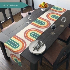 May include: A table runner with a retro rainbow design in shades of orange, yellow, green, and blue. The runner is 16 inches wide and 90 inches long and is made of polyester.