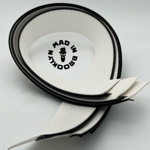 May include: Three white and black fabric strips with a stitched edge. The strips are rolled up and have a black circle with the text "MAD IN BROOKLYN" and a small cartoon image of a man with a beard and a hat.