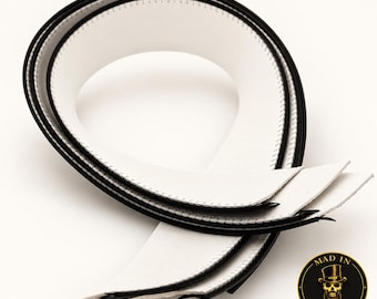 May include: A coiled strip of white material with black edges and visible black stitching along the borders. The strip is looped into a circular shape. A circular logo featuring a skull wearing a top hat and the text MAD IN BROOKLYN is present.