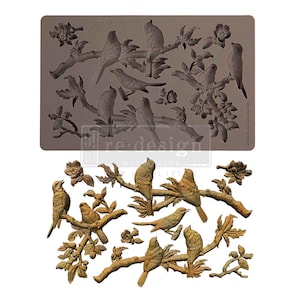 May include: A grey silicone mould featuring birds on branches and flowers. The mould is labelled "ITEM NO. 631661" and "WHISPERS OF WINGS". Below, a finished product in a bronze colour shows the same design.