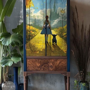 May include: A tall, dark blue cabinet with a painted scene of a yellow brick road leading to a castle. The cabinet has a wooden drawer and legs. The image on the doors depicts a person and a dog walking on the road.