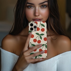 Op de afbeelding: Een telefoonhoesje met een crèmekleurige achtergrond en een patroon van rode kersen en groene bladeren. De hoes heeft een glanzende afwerking en een camera-uitsparing.