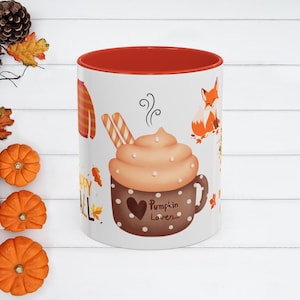 May include: White ceramic mug with a red interior, featuring a fall-themed design. The design includes a pumpkin spice latte, a fox, fall leaves, and the words "Happy Fall" and "Pumpkin Lover."