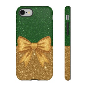 May include: A green and gold glitter phone case with a gold bow design. The top half of the case is green, and the bottom half is gold. The bow is centered on the case. The side of the case is also green and gold.
