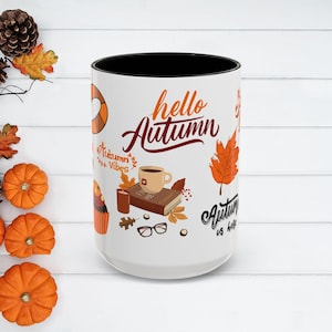 May include: White ceramic mug with a black interior, featuring the text "hello Autumn" in orange script. The mug is decorated with fall-themed illustrations, including a coffee cup, book, and leaves.